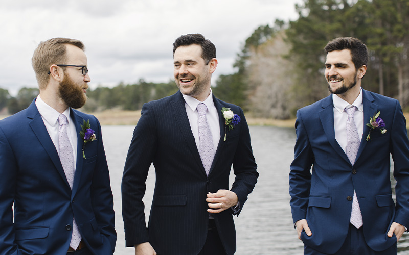 Blush Bridal and Formal Wear - Groom and groomsmen in navy blue suits on wedding day with boutonnieres and lavender ties